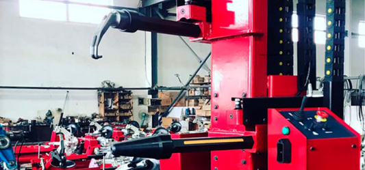 KATOOL WL70 Rim Straightener & Wheel Repair Machine in action showing its bright red hydraulic framework and precision control panel in a professional automotive workshop with additional equipment in the background.