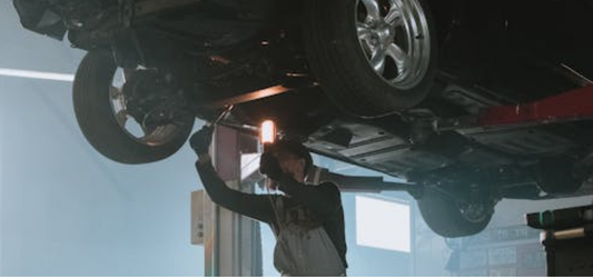 Mechanic performing maintenance under a car elevated on a two-post lift in an auto repair shop